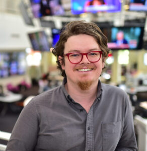 Photo of man with red glasses in grey shirt.