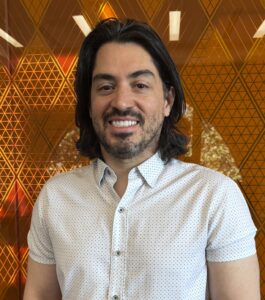 Headshot of man with long black hair in white short sleeve shirt.
