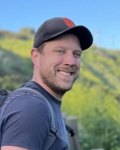 Headshot of a man smiling in a baseball cap.