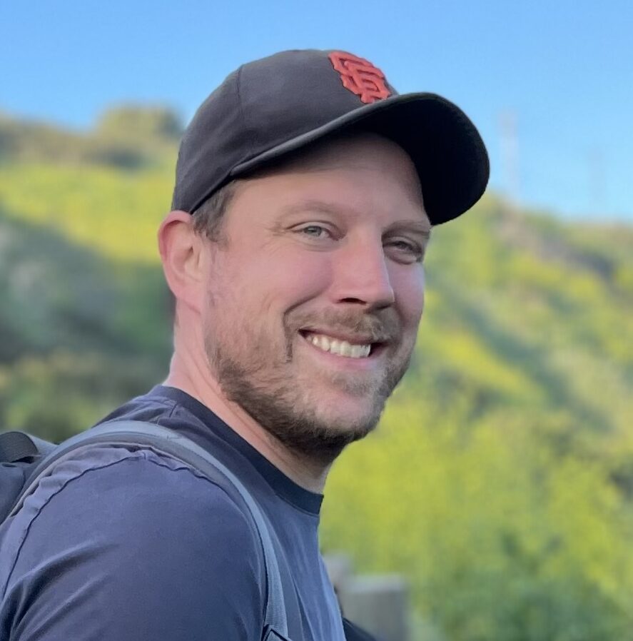 Headshot of a man smiling in a baseball cap.