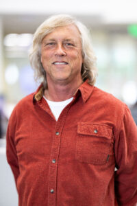 Photo of man with long white hair in an orange shirt.