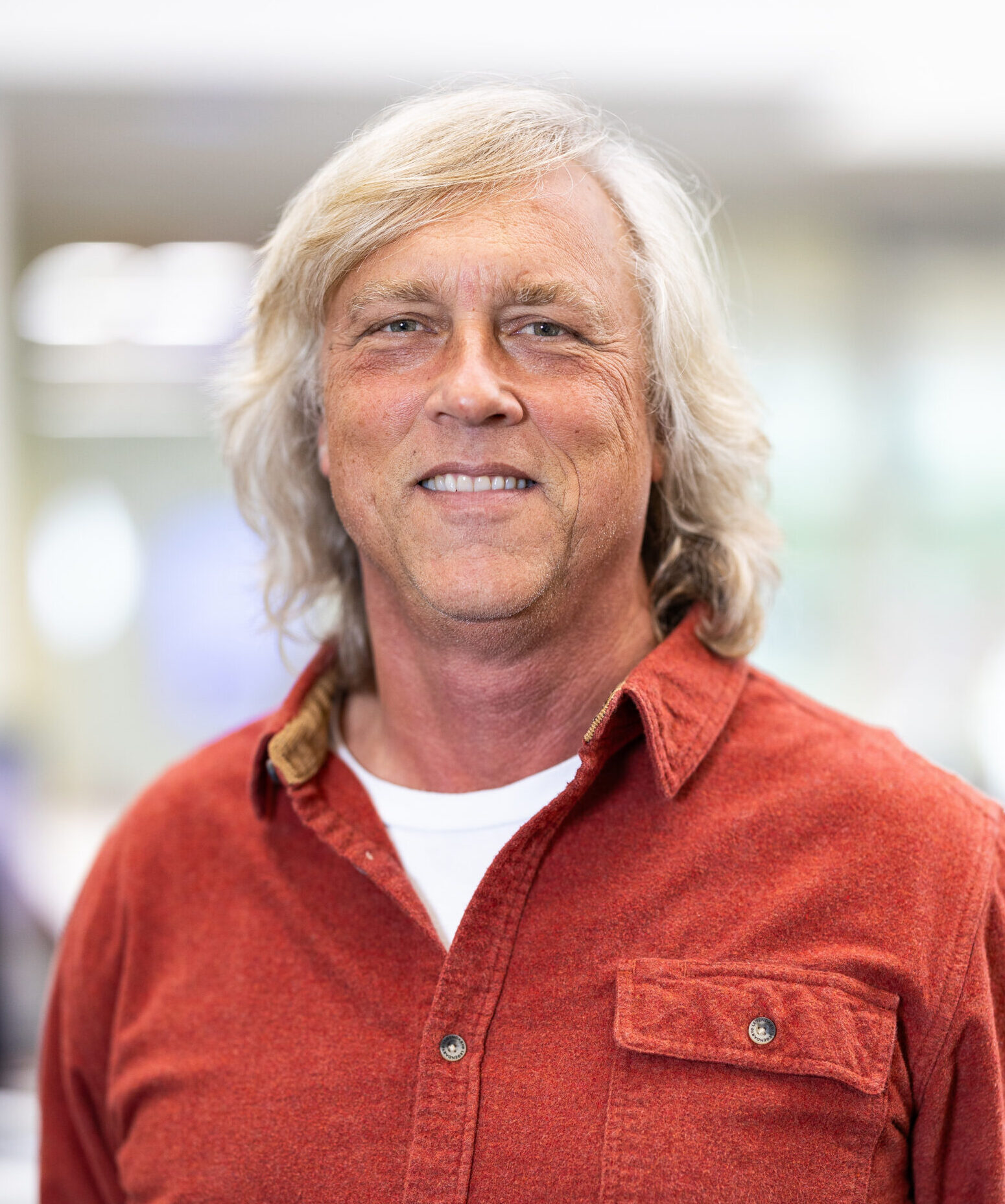 Photo of man with long white hair in an orange shirt.